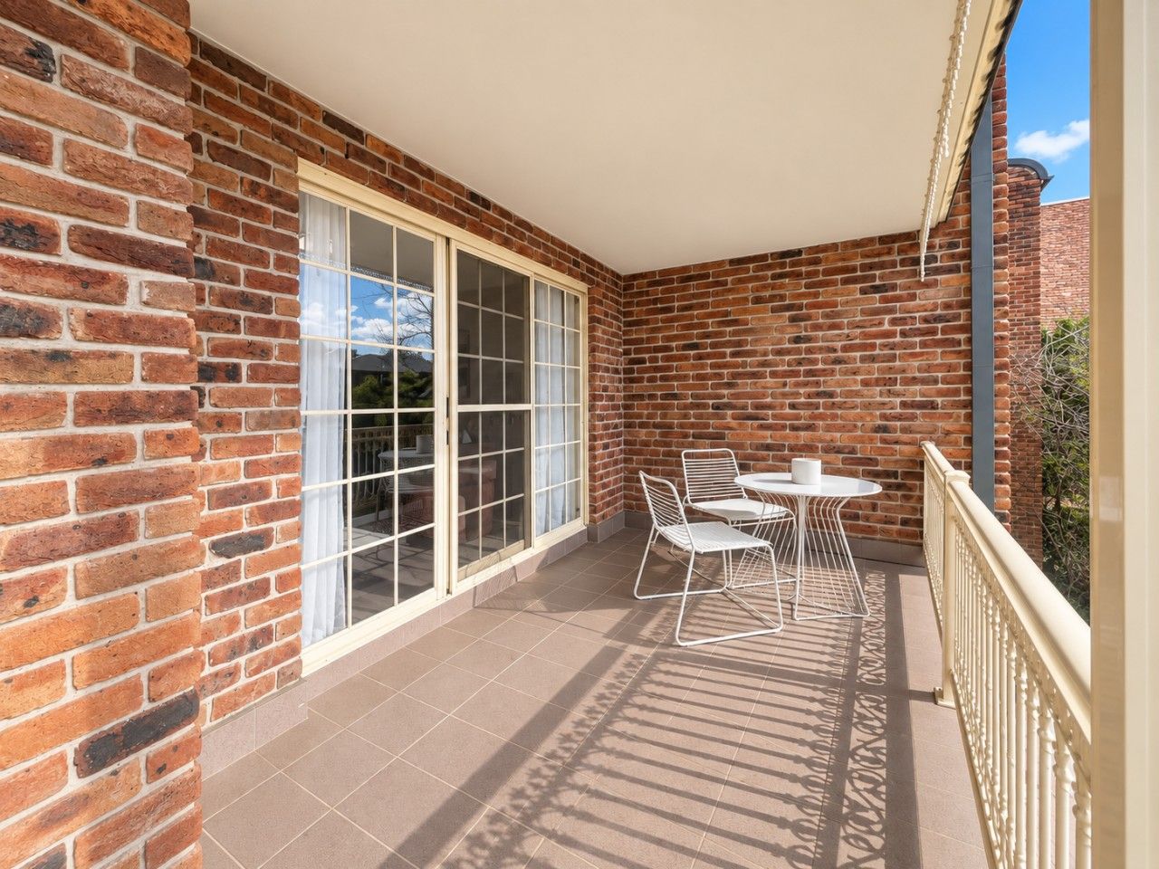 A balcony with a brick wall, a sliding glass door, and a table with chairs.