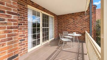 A balcony with a brick wall, a sliding glass door, and a table with chairs.