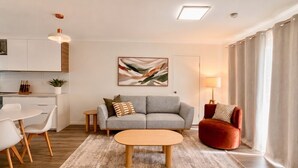 A modern living room with a sofa, a red armchair, a coffee table, and a dining area with chairs. - 2BR Inner South Stay with Pools, Gym and Sauna (Griffith)