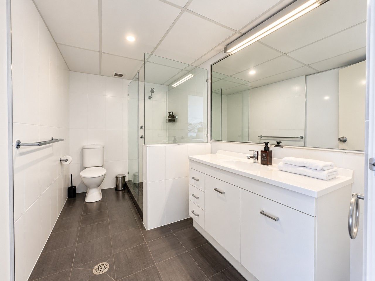A modern bathroom with a toilet, a glass-enclosed shower, and a white vanity with a mirror.
