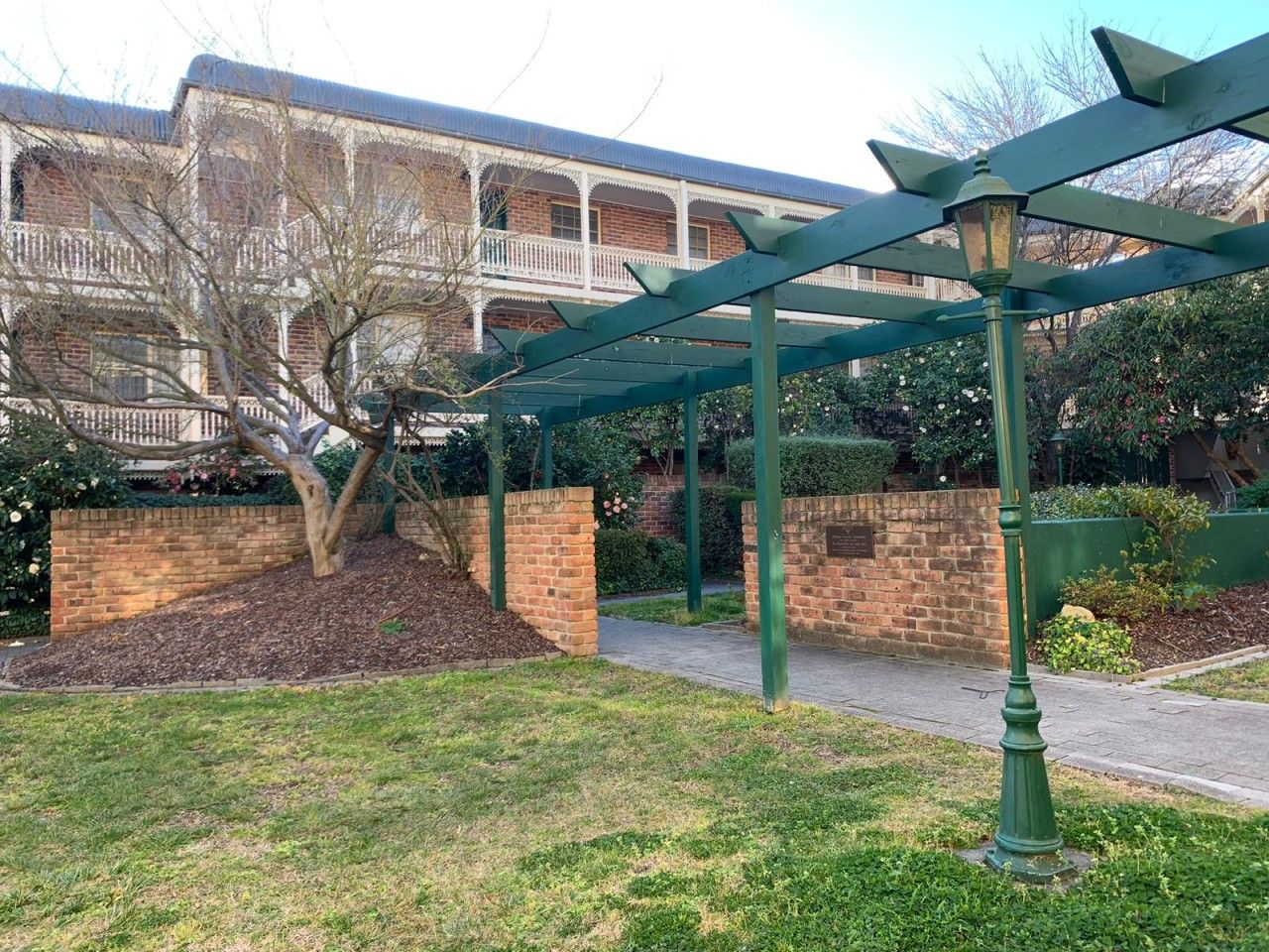 A courtyard with a brick wall, a tree, and a green pergola structure.