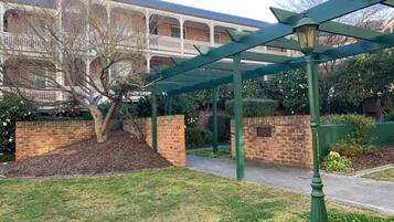 A courtyard with a brick wall, a tree, and a green pergola structure.
