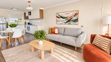 A modern living room with a sofa, coffee table, and a dining area with chairs and a table.
