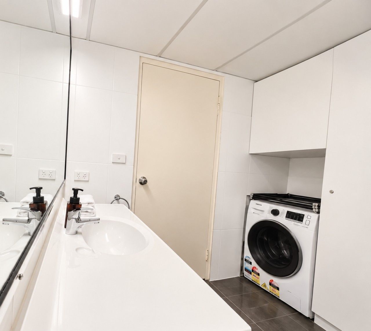 A bathroom with a sink, mirror, toilet, and a washing machine.