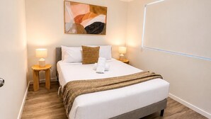 A neatly arranged hotel room with a bed, two bedside tables, a wall-mounted artwork, and a ceiling light. - 2BR Inner South Stay with Pools, Gym and Sauna (Griffith)