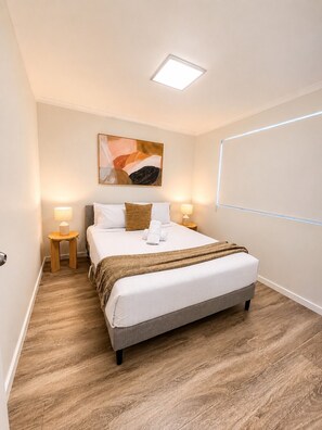A neatly arranged hotel room with a bed, two bedside tables, a wall-mounted artwork, and a ceiling light. - 2BR Inner South Stay with Pools, Gym and Sauna (Griffith)
