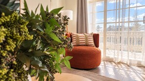 A cozy room with a round orange chair, a white lamp, and a view of a balcony with a lace railing. - 2BR Inner South Stay with Pools, Gym and Sauna (Griffith)
