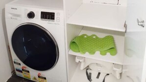 A laundry area with a Samsung washing machine, a shelf with a green mat, and a bottle of liquid soap. - Contemporary 2BR Apt in Kingston (Griffith)