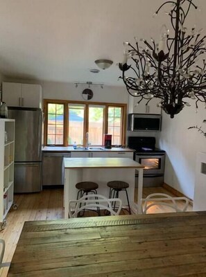 A compact kitchen with a central island, a refrigerator, a microwave, and a stove. There are two stools at the island and a window with a view of the outside.