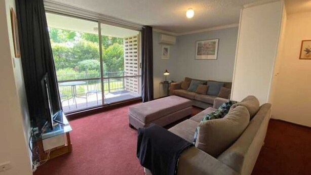 A living room with a sofa, ottoman, and a television on a stand. - Quiet 2BR Apartment with Garden views in Griffith (Griffith)