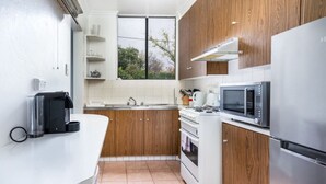 A compact kitchen with wooden cabinets, a white countertop, a stainless steel refrigerator, a microwave, and an oven. - Quiet 2BR Apartment with Garden views in Griffith (Griffith)