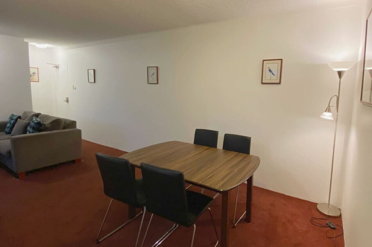 Huoneessa on puinen pöytä ja neljä tuolia, sohva sekä lattialla seisova jalkalamppu.