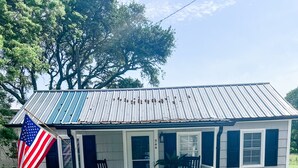 Una casa a un piano con tetto in metallo, un portico con ringhiere bianche e una bandiera americana.