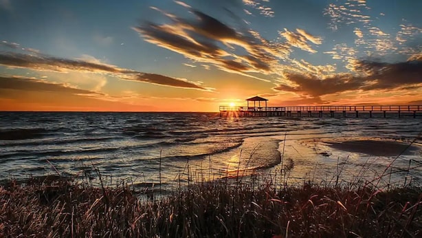 Un molo che si protende nell'oceano al tramonto, con una piccola costruzione all'estremità.