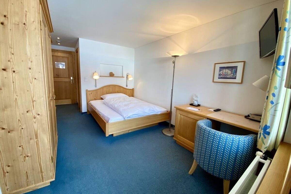 Une chambre à coucher avec un lit en bois, un bureau avec une chaise, une lampe sur pied et un téléviseur fixé au mur.