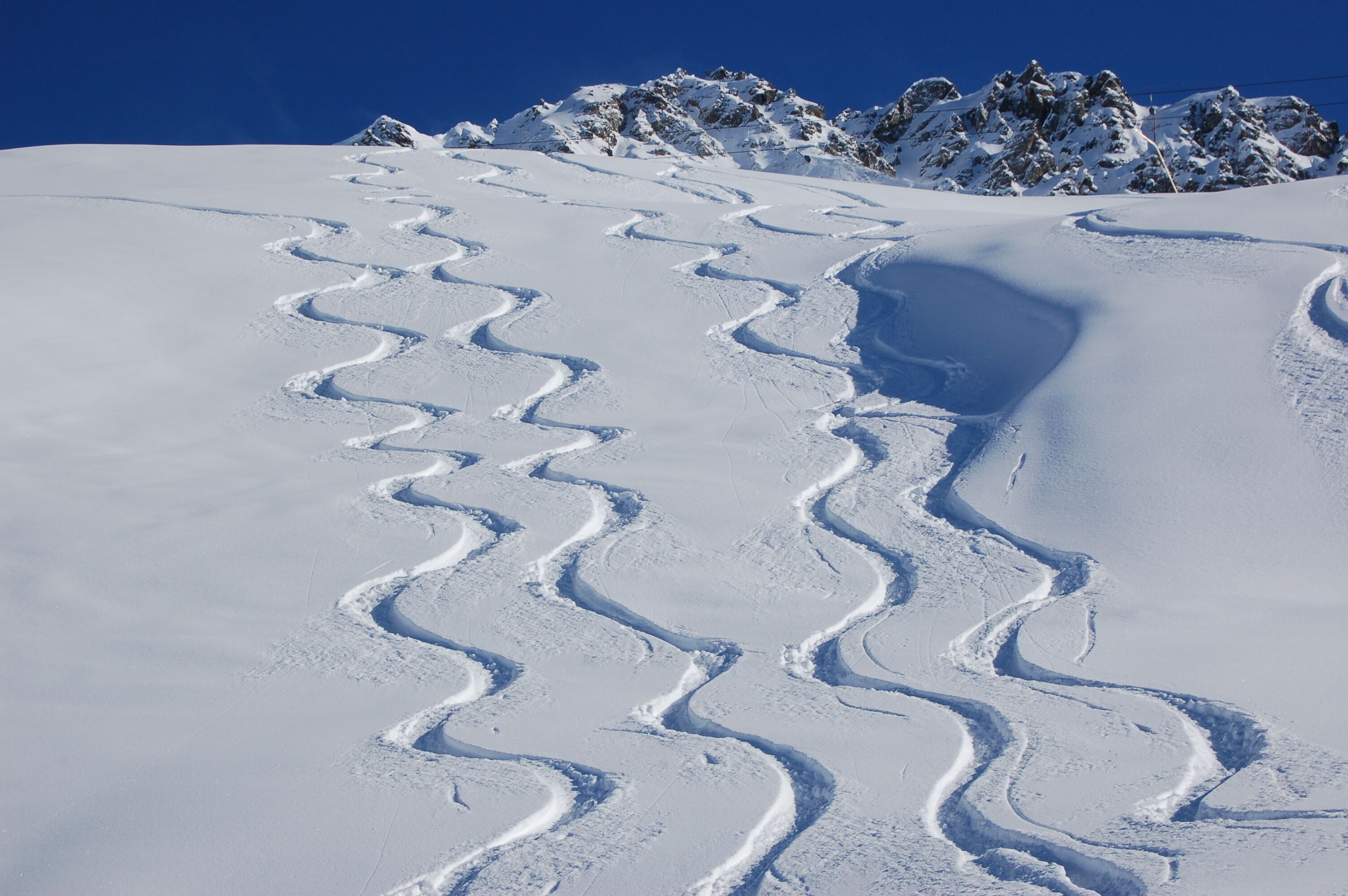 A snow-covered ski trail with a clear sky and distant mountains.