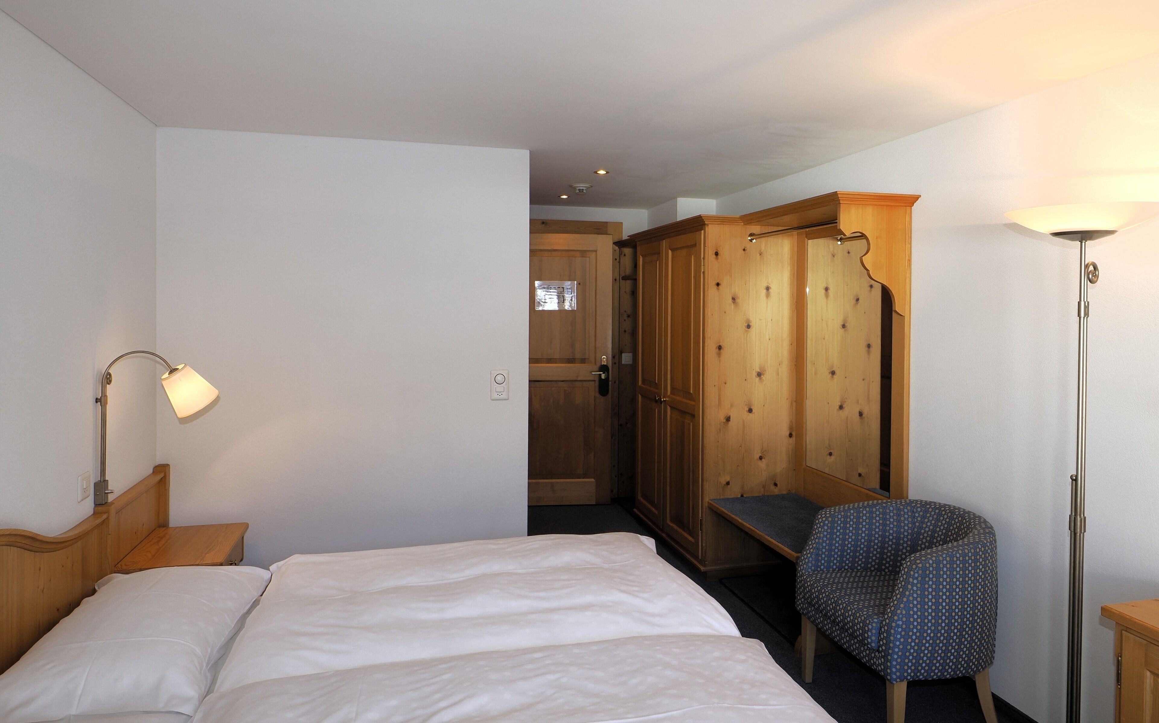 Ein Schlafzimmer mit Bett, Sessel, Kleiderschrank und Lampe.
