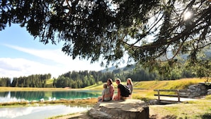 A group of people sitting on a rock by a lake with a wooden bench and a stone wall in the background. - Hotel Alpina Parpan (Churwalden)