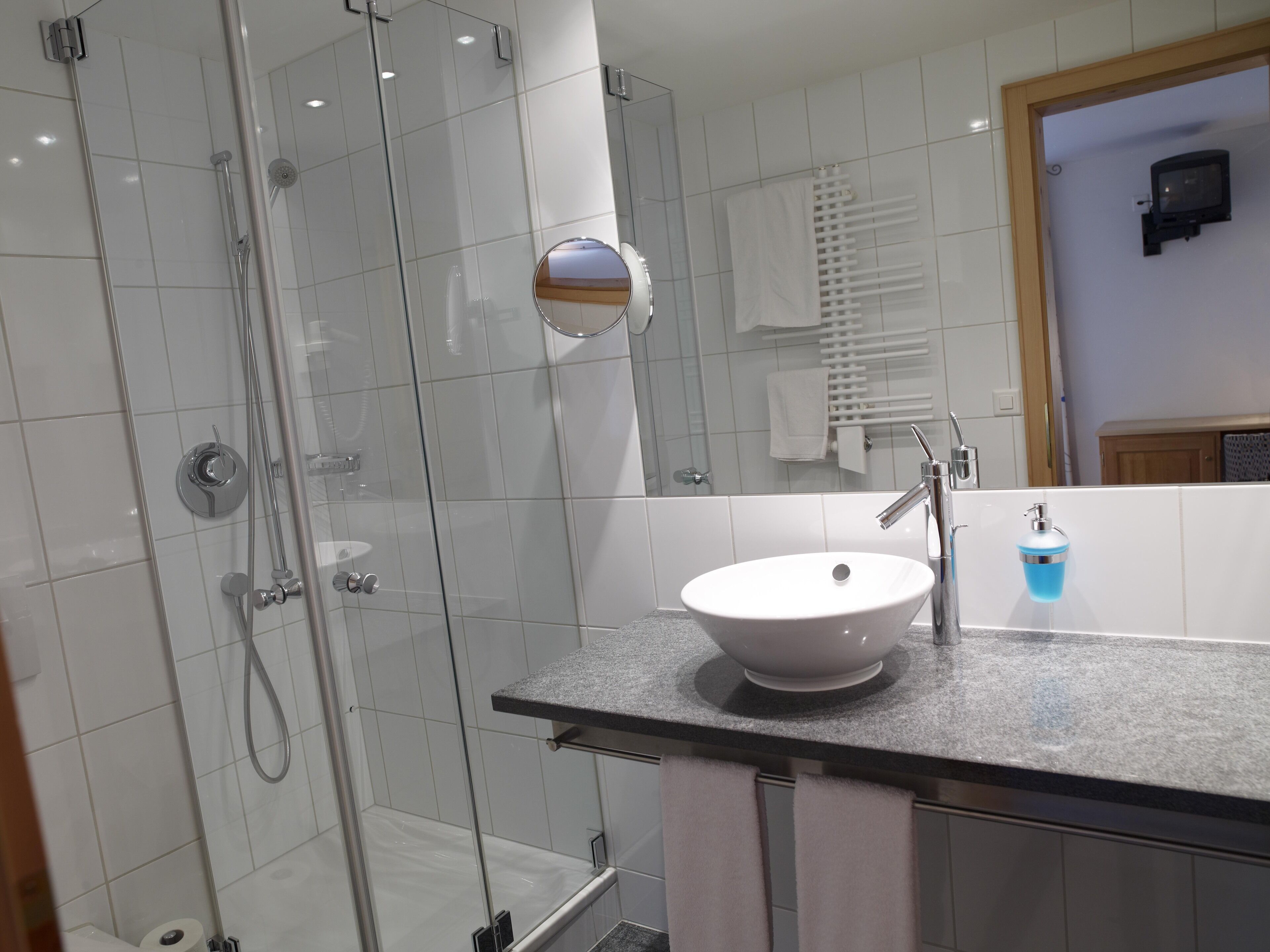 Un baño moderno con ducha de vidrio, lavamanos blanco y barra para toallas.