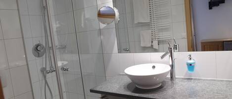 Un baño moderno con ducha de vidrio, lavamanos blanco y barra para toallas.