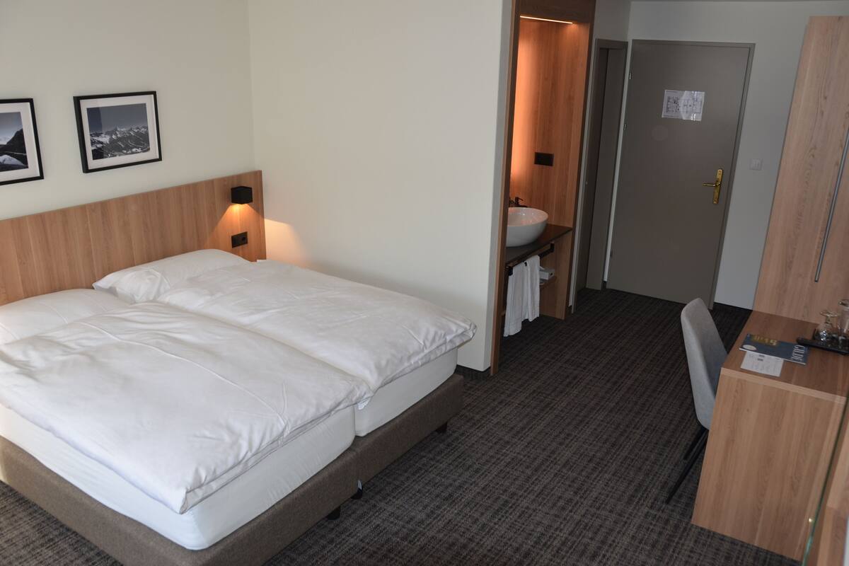 Une chambre d’hôtel avec un grand lit, un bureau, une salle de bain avec un lavabo et des tableaux encadrés accrochés au mur.