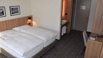 A hotel room with a large bed, a desk, a bathroom with a sink, and framed pictures on the wall.
