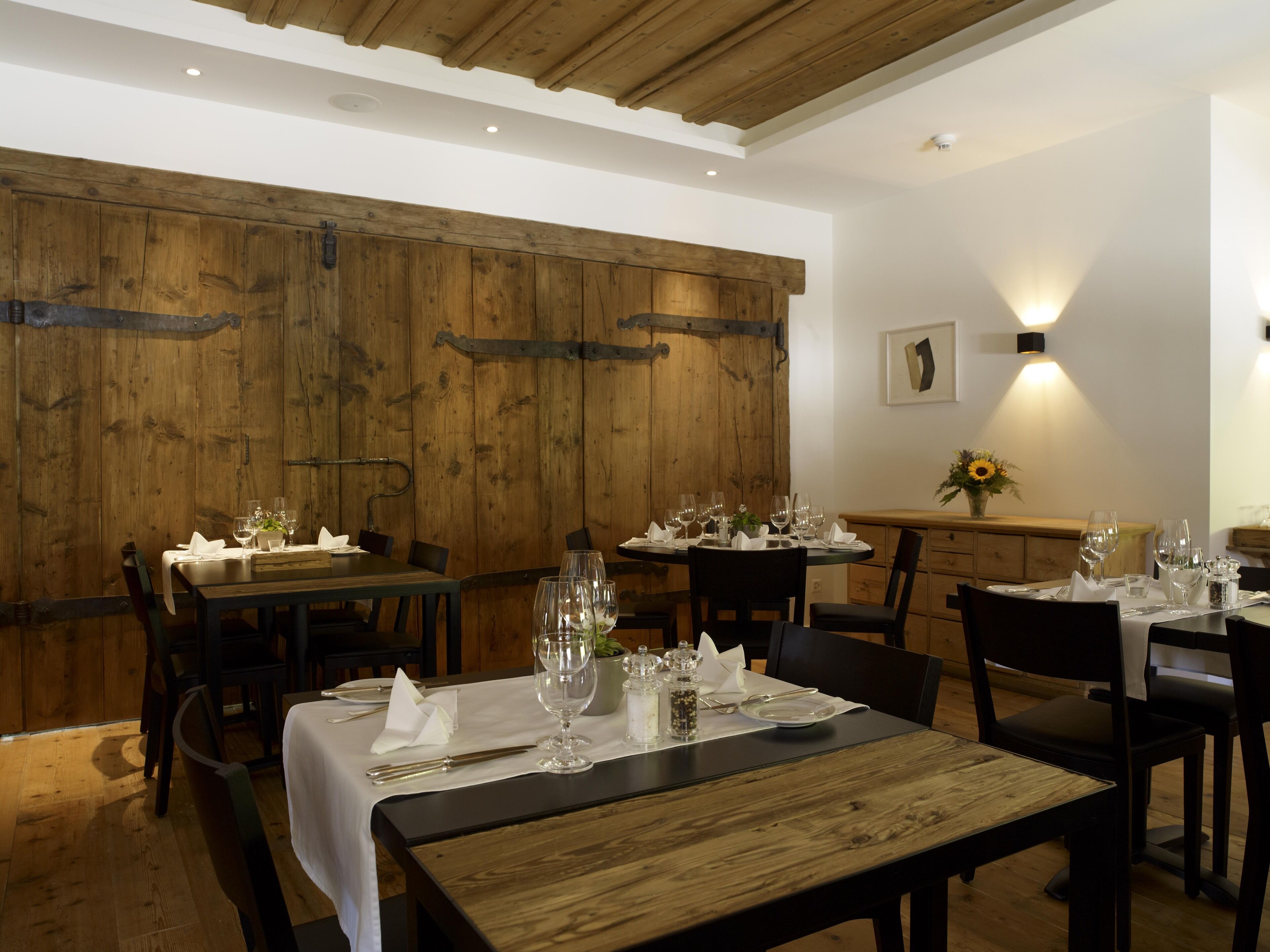 A restaurant with wooden walls, tables set for dining, and a vase with flowers on the sideboard.