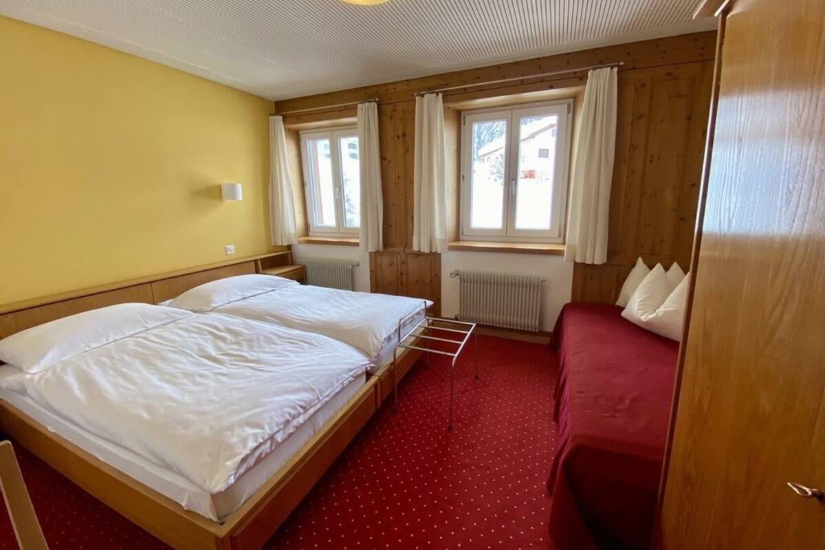 Une pièce avec deux lits, un canapé rouge, des murs en bois et de grandes fenêtres avec des rideaux.