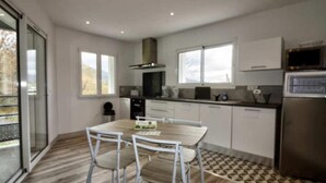 A modern kitchen with white cabinets, a stainless steel refrigerator, and a dining table with four chairs. - T2, Maison Harriondoa (Cambo-les-Bains)