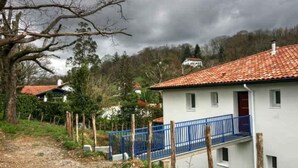 A white building with a red-tiled roof, a blue balcony, and a gravel path leading to it. - T2, Maison Harriondoa (Cambo-les-Bains)