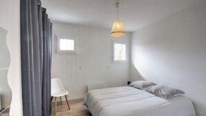 A bedroom with a bed, two windows, a chair, and a hanging light fixture. - T2, Maison Harriondoa (Cambo-les-Bains)
