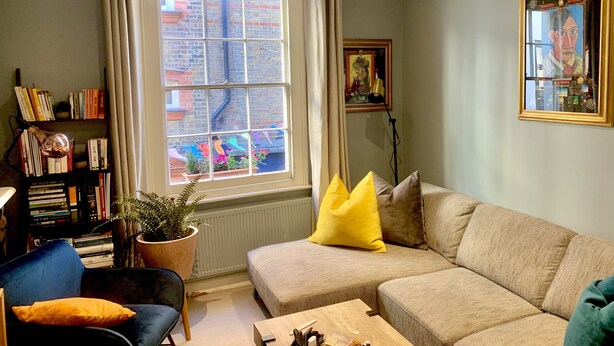A living room with a sofa, a chair, a bookshelf, a window with curtains, and a radiator.