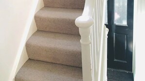 A carpeted staircase with white balusters and a black door at the bottom.