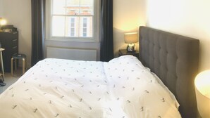 A bedroom with a bed, a window with curtains, a lamp, and a radiator.