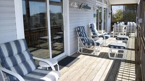 A covered outdoor seating area with striped lounge chairs and tables, a ceiling fan, and a view through glass doors.