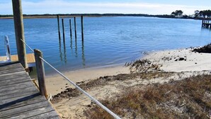 A wooden dock extending into calm water, surrounded by sandy beach and sparse vegetation.