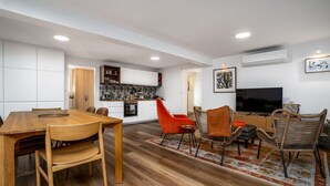 Un espace de vie moderne comprenant une table à manger en bois, des chaises orange, un téléviseur et un coin cuisine.