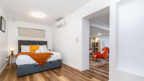 Une chambre moderne avec un lit, une table de chevet et une chaise rouge dans la pièce adjacente.