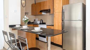 Eine moderne Küche mit Holzschränken, einem Edelstahlkühlschrank, einer schwarzen Arbeitsplatte und einem Essbereich mit zwei Stühlen.
