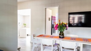 Un espace de salle à manger moderne, avec une longue table, des chaises blanches et un vase rempli de fleurs.