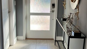 A hallway with a frosted glass door, a console table with decorative items, and a tiled floor. - Luxury/Modern 5Bed and 4bath Private Pool and Free Resort 10min da Disney 11ppl (Kissimmee)