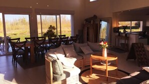 A spacious living room with a large window, a sofa, a coffee table, and a dining area with chairs. - House on large terrain between beach & salt marshe (La Couarde-sur-Mer)