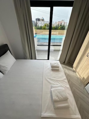 Une chambre d’hôtel avec un lit, une vue sur une piscine et sur le paysage urbain.
