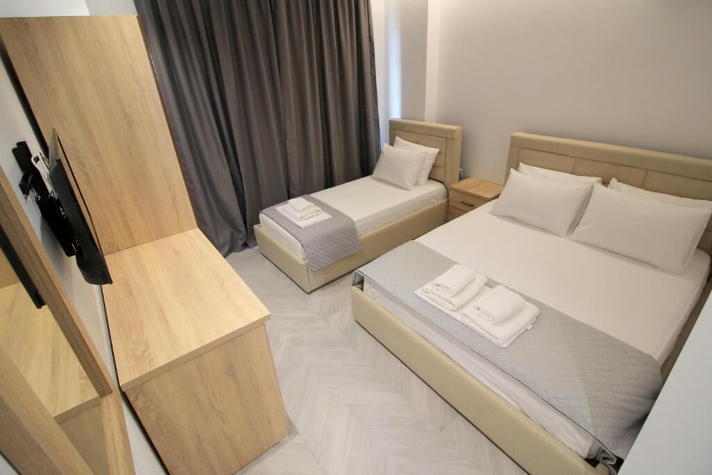 Quarto de hotel com duas camas, um guarda-roupa de madeira, uma escrivaninha e uma janela com cortinas.