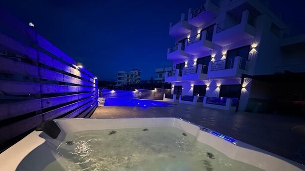 A hot tub with water jets, surrounded by a pool and a building with balconies. - Noa Boutique Hotel (Ksamil)