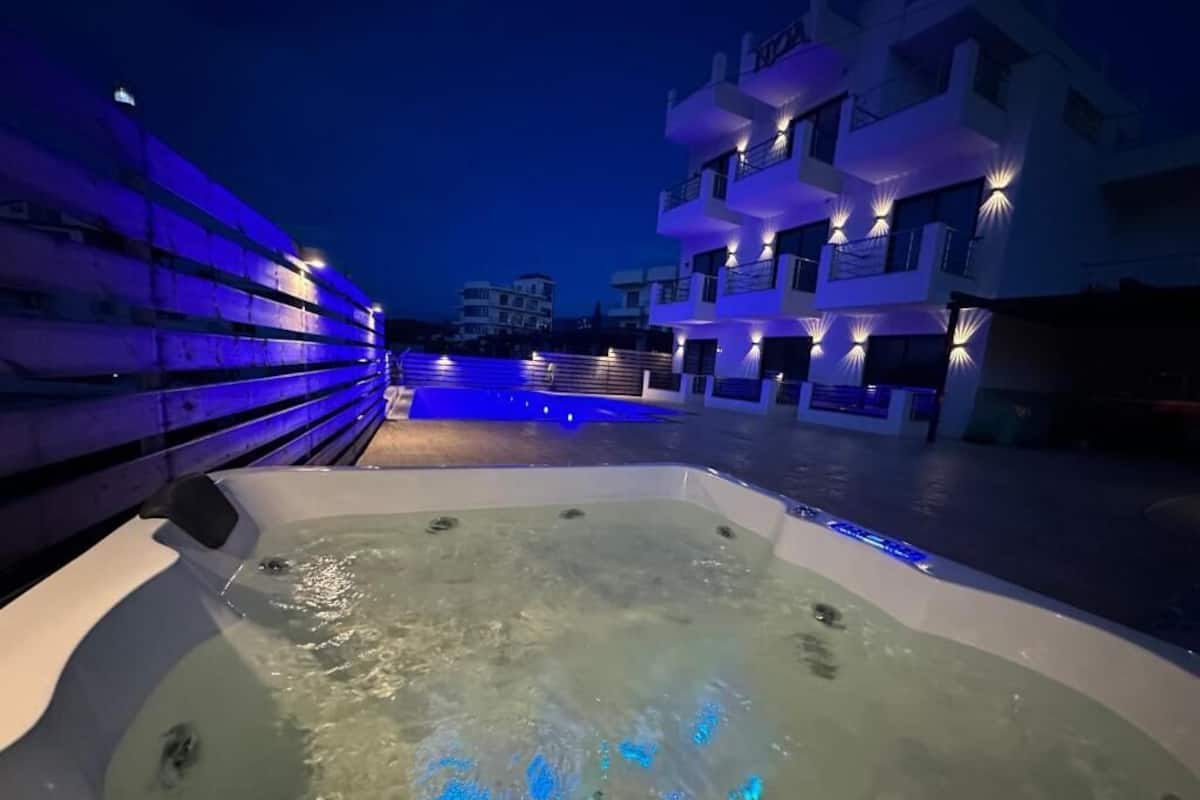 A hot tub with water jets, surrounded by a pool and a building with balconies.