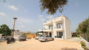 A modern two-story building with a balcony, parked cars, and a dirt driveway. - Noa Boutique Hotel (Ksamil)