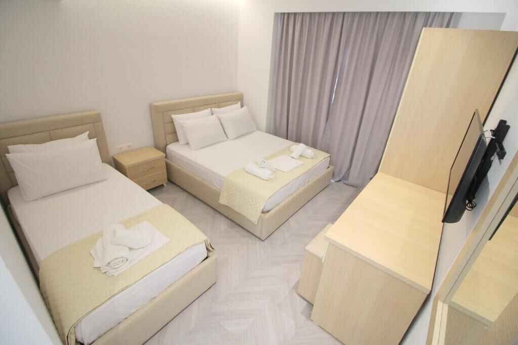 Une chambre d’hôtel avec deux lits, une commode en bois, une télévision et une fenêtre avec des rideaux.