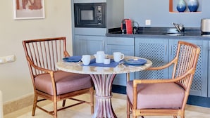 Una cocina con una mesa de comedor, dos sillas de mimbre, un microondas y una cafetera.