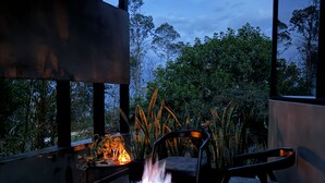 A modern outdoor seating area with a fire feature, surrounded by large windows and lush greenery. - Almazewá (Ubaque)